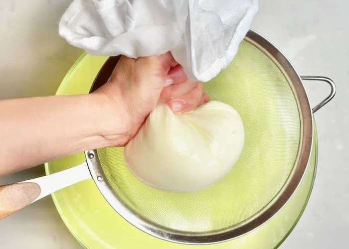 Откиньте получившуюся массу на свернутую в 4 слоя плотную марлю и дайте стечь лишней жидкости. Периодически перемешивайте столовой ложкой, чтобы сыворотка стекала лучше.