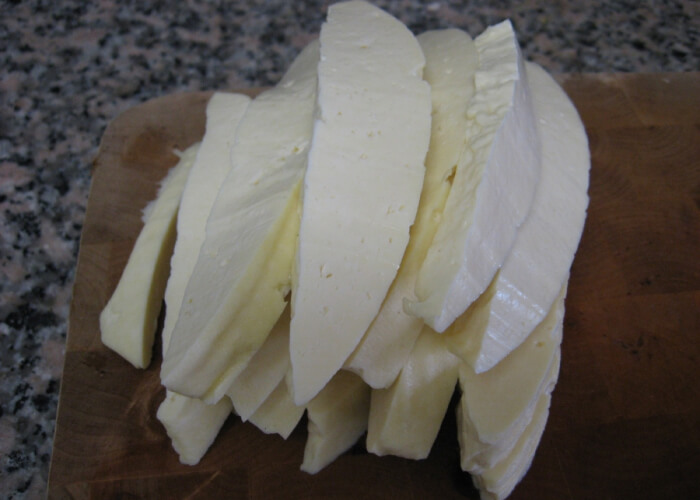 Подготовленный сыр достаньте из-под гнета, нарежьте полосками толщиной до 1,5-2 см и сложите в кастрюлю. Подогрейте воду или сыворотку, если она осталась – понадобится примерно 2-3 чашки. Жидкость температурой не выше 80 градусов нужно аккуратно и постепенно влить в кастрюлю с сыром, периодически помешивая ее содержимое. В итоге должна получиться достаточно густая масса, которую нужно вымесить так же, как вы вымешиваете тесто.