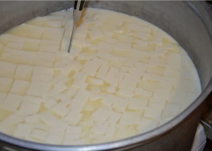 Теперь нужно резать сгусток из молока таким образом, чтобы получились кубики со стороной 1,5-2 см. После этого аккуратно вымешайте массу до отделения зерна. Если свернувшееся молоко начало остывать, поместите кастрюлю в водяную баню, но следите, чтобы температура сгустка не превышала 34 градуса